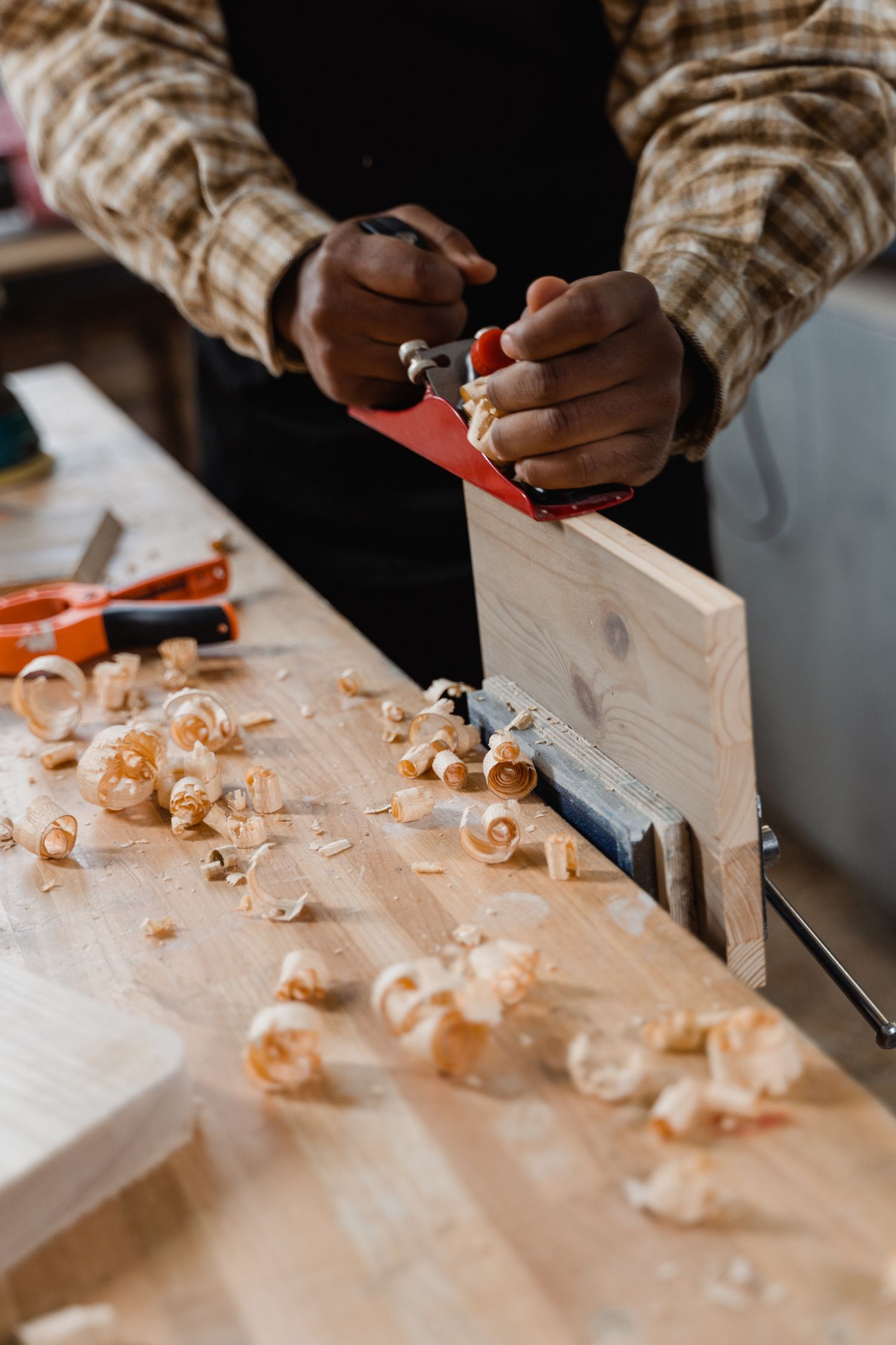 Artisan menuisier qui rabote une planche de bois dans son atelier